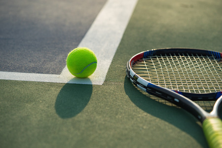 Tennis ball and racket under late evening sunlight