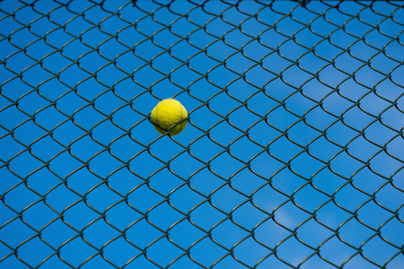Tennis ball on metal wire against blue sky. Concept of tennis protection equipmentの写真素材