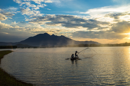 Dong Mo lake with a couple of fishers catching fish by net trap in beautiful sunset period in Son Tay town, Hanoi, Vietnamの写真素材