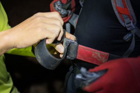 Man hand tightening rock climbing equipments with rope, hook, belt in dark cave in Son Dong, the largest cave in the worldの写真素材