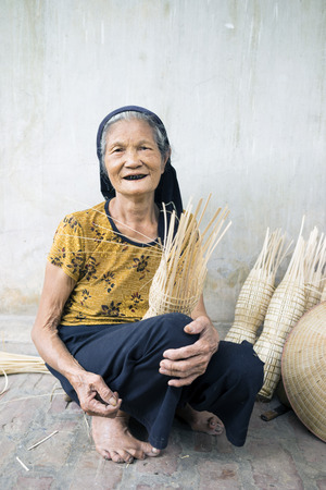 Hung Yen, Vietnam - July 26, 2015: Old woman weaves bamboo fish trap at Vietnamese traditional crafts village Thu Sy, Hung Yen province.のeditorial素材