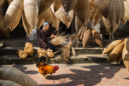 Hung Yen, Vietnam - July 9, 2016: Old house yard with many bamboo fish trap, a cock, and female craftsman making traditional bamboo fish trap at her old house in Thu Sy trade villageのeditorial素材