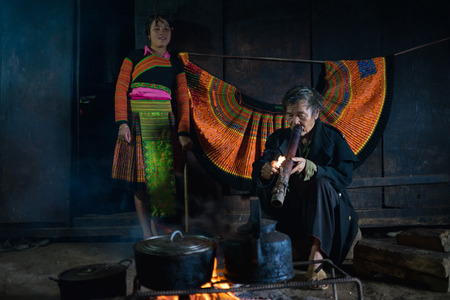 Son La, Vietnam - Jan 13, 2016: H'mong man smokes next to the fire and his granddaughter inside his house in Bac Yen districtのeditorial素材