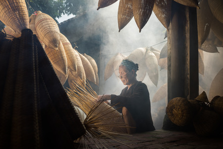 Hung Yen, Vietnam - July 9, 2016: Old house yard with many bamboo fish trap and female craftsman making traditional bamboo fish trap at her old house in Thu Sy trade villageのeditorial素材