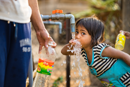 Kon Tum, Vietnam - Mar 29, 2016: A little girl drink water from outdoor tap which water supplied by drilling well in Central Highland of Vietnam. Fresh water is problem in underdevelopment regionのeditorial素材