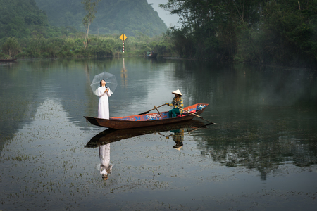 Ninh Binh, Vietnam - Oct 9, 2016: River scene with tourist boat carrying girls wearing traditional dress Ao Dai, conical hat, and flower.のeditorial素材