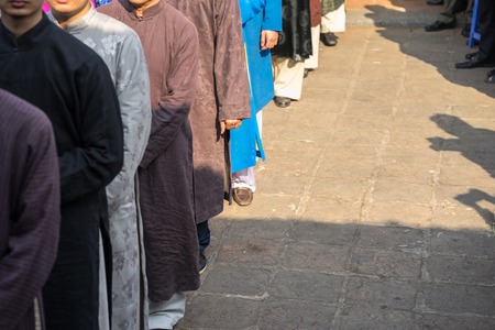 Vietnamese men wear traditional long dress Ao Dai standing at ancient village communal house....