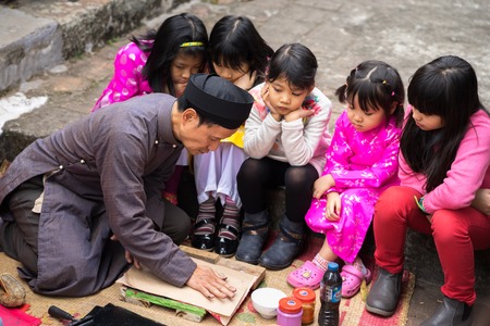 Hanoi, Vietnam - Jun 22, 2017: Old Dong Ho village artist making Dong Ho folk woodcut painting with children surrounded in communal house, Quoc Oai district. Concept of cultural preservationのeditorial素材