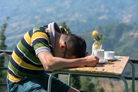 Young man sleeping outdoor with his head leaning on coffee table.の写真素材