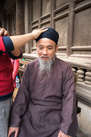 Hanoi, Vietnam - Jun 22, 2017: Old man with ancient feudal traditional long dress Ao Dai for his feudal official role in communal house at So village, Quoc Oai district.のeditorial素材