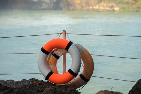Orange lifebuoy hanging on a column in a park near the lakeの写真素材