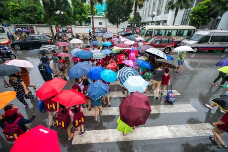Hanoi, Vietnam - Aug 24, 2017: Busy street with crowded people using umbrella in rainy morning on a...