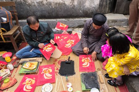 Hanoi, Vietnam - Jun 22, 2017: Old Dong Ho village artist making Dong Ho folk woodcut painting with children surrounded in communal house, Quoc Oai district. Concept of cultural preservationのeditorial素材