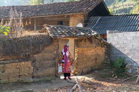 Ha Giang, Vietnam - Nov 26, 2018: Lo Lo ethnic minority woman in traditional costume with old wall-thicked house at Lo Lo Chai village, Dong Van districtのeditorial素材
