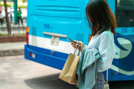 Asian young girl use smartphone waiting for bus at bus stop
