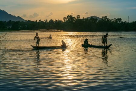 Fisher men fishing on a fishing boat in river in Mekong Delta on floating water season at sunsetの写真素材