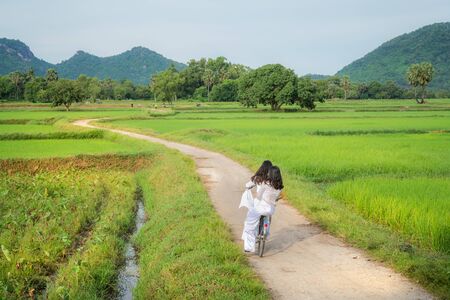 Rural landscape in Vietnam countryside with Vietnamese women wearing traditional dress Ao Dai cycling on the roadの写真素材