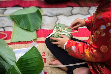 Child wear traditional dress Ao Dai learning to make Chung cake by hands closeup, Chung cake is the most important traditional Vietnamese lunar New Year (Tet) food.の写真素材