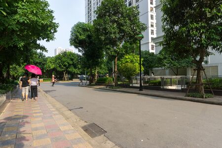 Urban walking road among green tree in modern apartment buildings in big city. People walking on the pathの写真素材