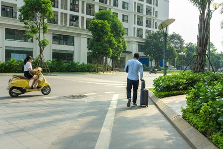 Urban walking road among green tree in modern apartment buildings in big city, with a man walk pulling luggageの写真素材