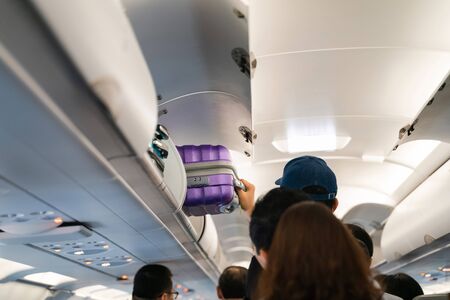 Hand take off hand luggage. Bag cabin on top shelf in airplaneの写真素材