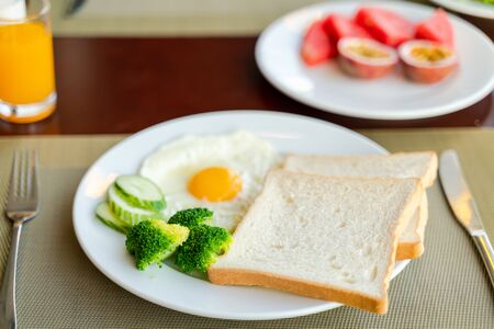 Fresh romantic breakfast table next to window with bread, fruit, juice, milk, egg, vegetable...