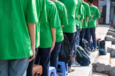 Queue of Asian teenagers in green t-shirt uniform standing in lineの写真素材