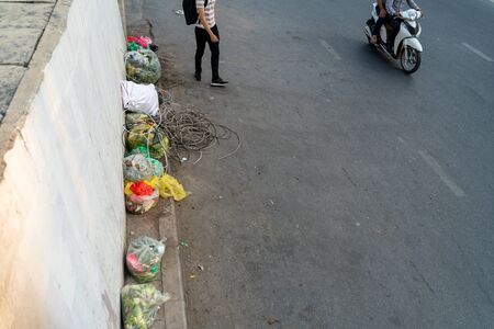 Pile of garbage bags and messy trash on street sidewalk with traffic on background in Hanoi, Vietnamの写真素材