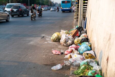 Pile of garbage bags and messy trash on street sidewalk with traffic on background in Hanoi, Vietnamの写真素材