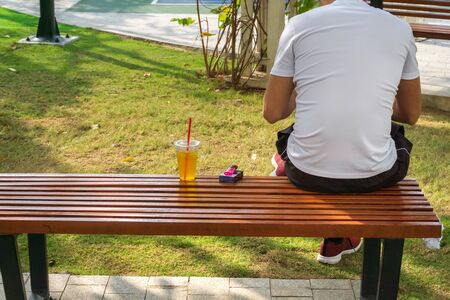 Young man sits on a park bench with a cup of tea and cigarette boxの写真素材