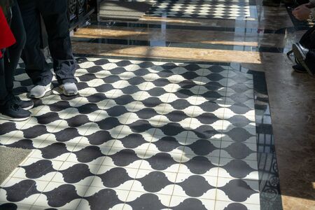 Black and white checkered floor grunge tiles marble surface at public place with interiors and people legsの写真素材