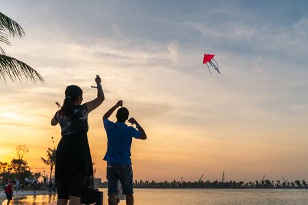 Silhouette Asian family members play kite by urban lakeの写真素材