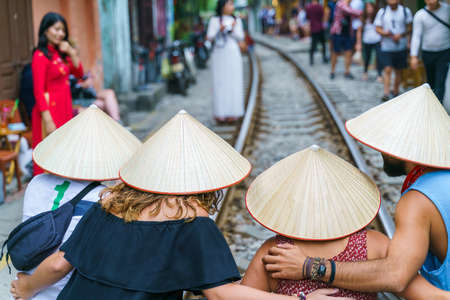 Foreign tourists with Vietnamese conical hats taking photo at narrow train railroad in old town in Hanoiのeditorial素材