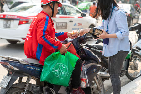 Hanoi, Vietnam - Mar 21, 2019: Now bike delivery man giving drinks and foods to recipient at Dao Tan streetのeditorial素材