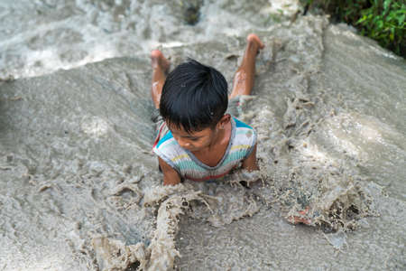 Chau Doc, Vietnam - Oct 13, 2018: Young boy child playing in the mud puddle on a summer day