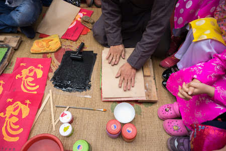 Hanoi, Vietnam - Jun 22, 2017: Old Dong Ho village artist making Dong Ho folk woodcut painting with children surrounded in communal house, Quoc Oai district. Concept of cultural preservationのeditorial素材