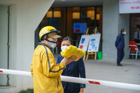 Hanoi, Vietnam - Apr 1, 2020: Courier in protective mask delivers goods to customer at Viet Phap hospital during covid-10 coronavirus outbreak pandemicのeditorial素材