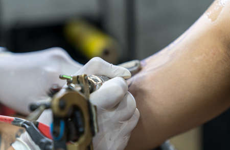 Tattoo artist in white gloves making a tattoo on man armの写真素材