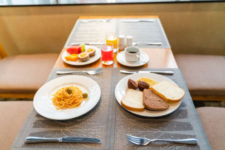 Fresh romantic breakfast table next to morning briliant light window, with bread, pastry, spaghetti, fruit, juiceの写真素材