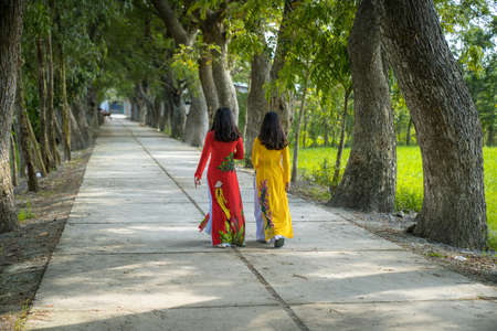 Vietnamese women in traditional dress (Ao Dai) walking on the rural road among treesの写真素材