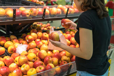 Hands of female buyer choosing red apples in supermarketの写真素材