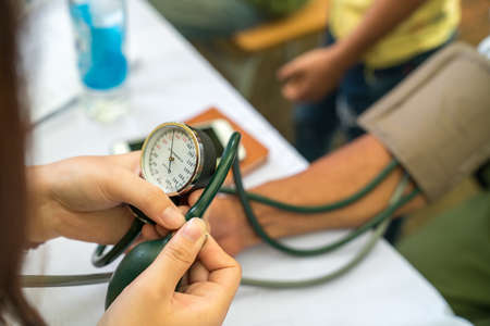 Volunteer nurse measuring blood pressure of poor Asian people outdoors closeupの写真素材