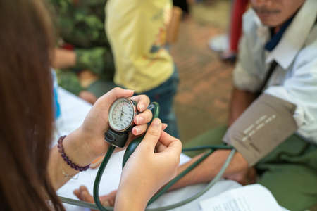 Volunteer nurse measuring blood pressure of poor Asian people outdoors closeupの写真素材