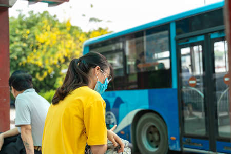 Asian young girl use smartphone waiting for bus at bus stop