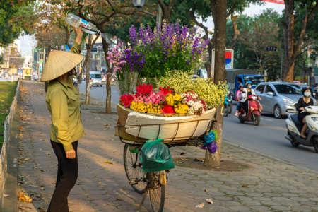 Flower basket on bike of street vendor on Hanoi street. Yellow leaf trees. Autumn or winter seasonの写真素材