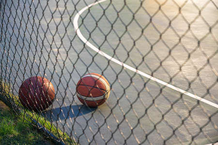 Basketball ball on illuminated playground at night with metal net on foregound.の写真素材