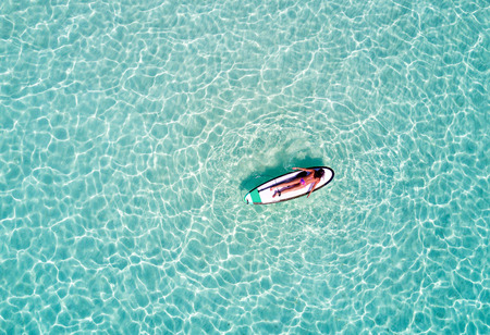 Aerial picture of a woman on a surfboard in turquoise waters in the Maldivesの写真素材