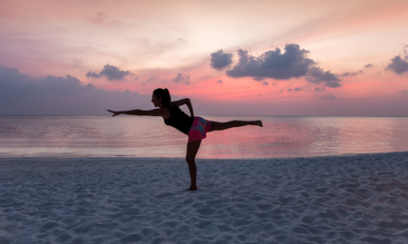 Woman doing yoga on a tropical beach during sunsetの写真素材