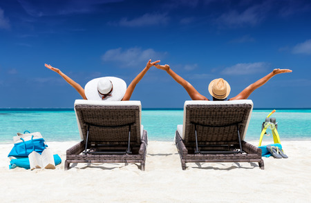 Happy couple in sunbeds enjoys their vacation on a tropical beach with turquoise watersの写真素材
