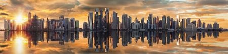 Panoramic view of the modern skyline of Doha, Qatar, at sunset time with reflection in the waterの写真素材
